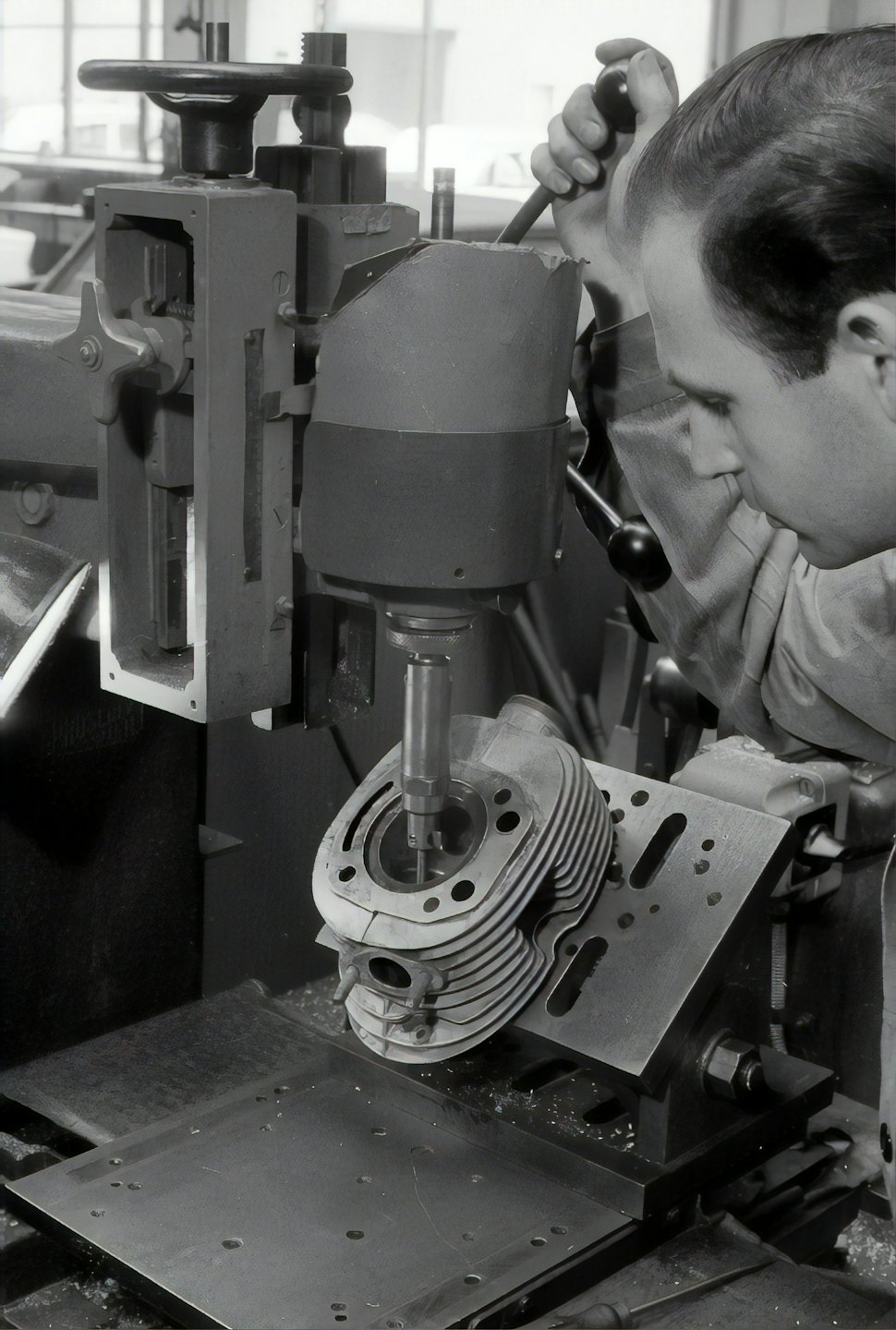 Man operating an industrial drill press on engine cylinder head.