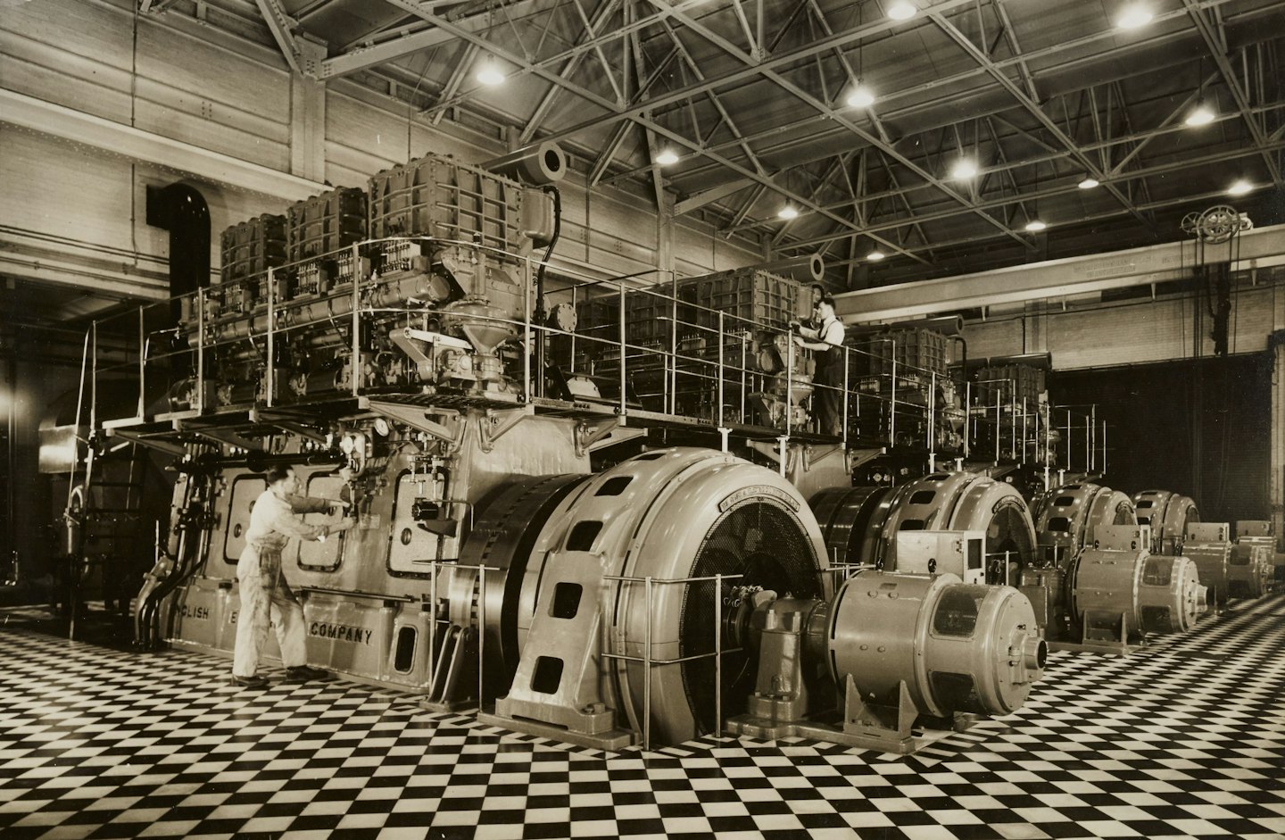 Two engineers repair large industrial machinery inside a spacious factory.